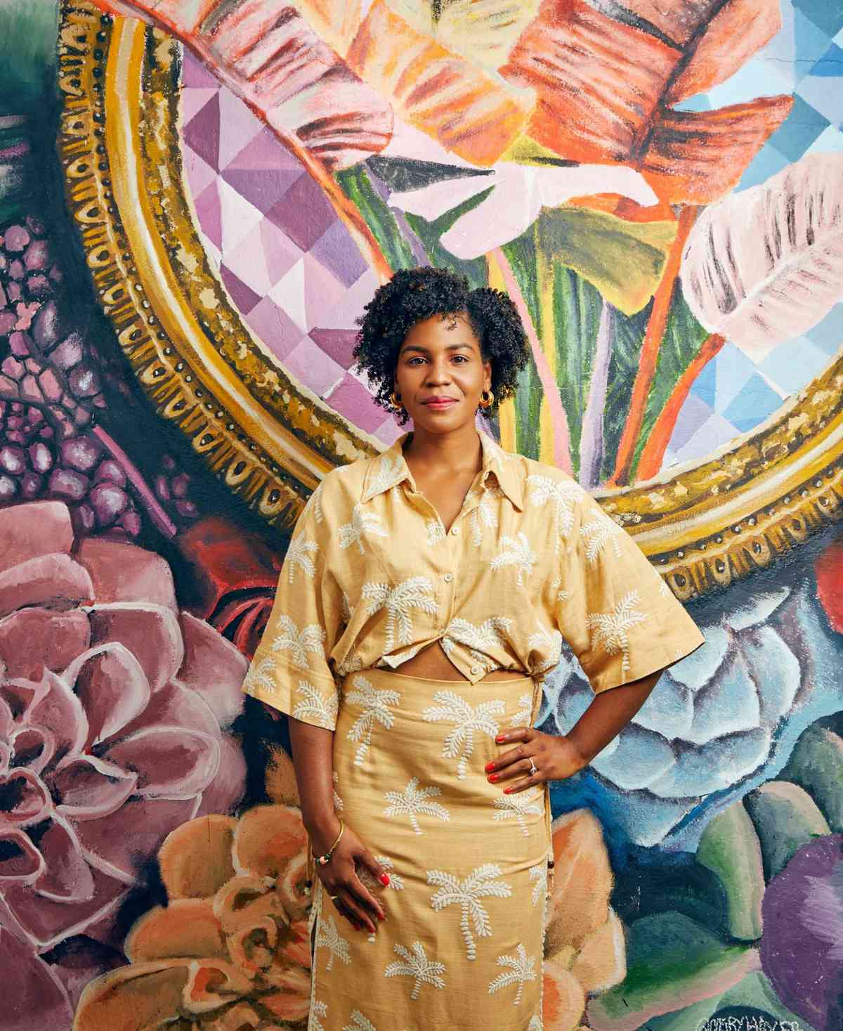Hotelier Jamila Ross wears a palm print top and skirt in front of a color mural at her hotel, the Copper Door B&B, in Miami