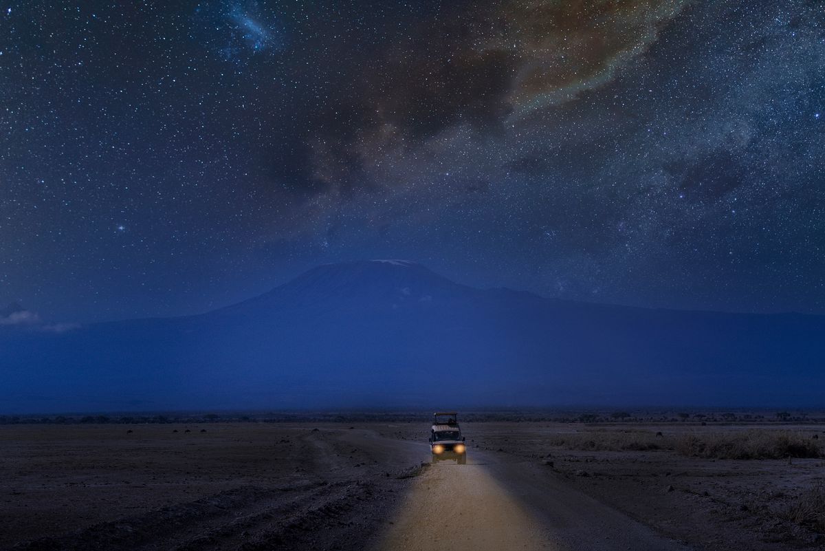 Front view of a four wheel drive vehicle on a dirt road under Mount Kilimanjaro in a starry night with Milky Way.
