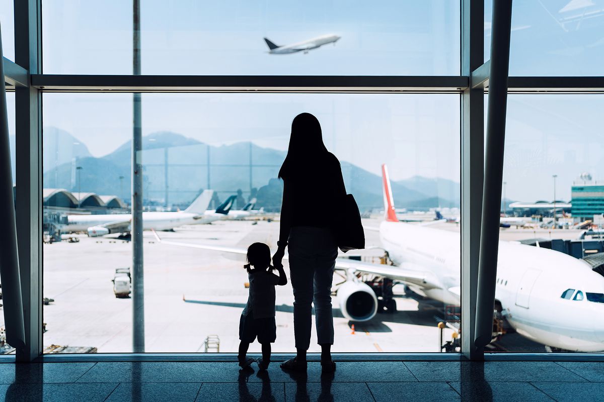 A mother holding hands daughter looking at airplane through window at the airport while waiting for departure