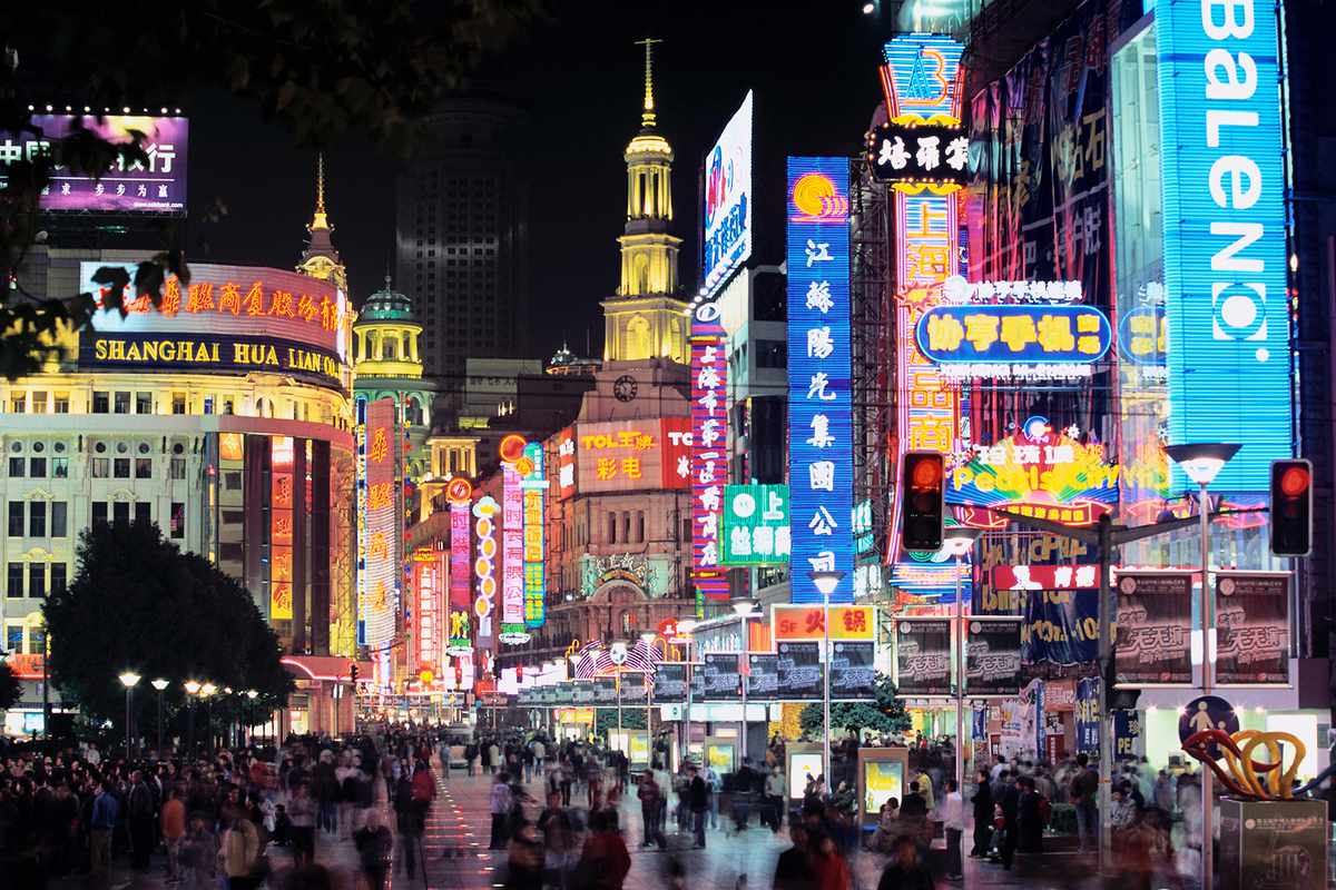 Bright neon lights, stores, and shoppers on Nanjing Road in Shanghai at night.