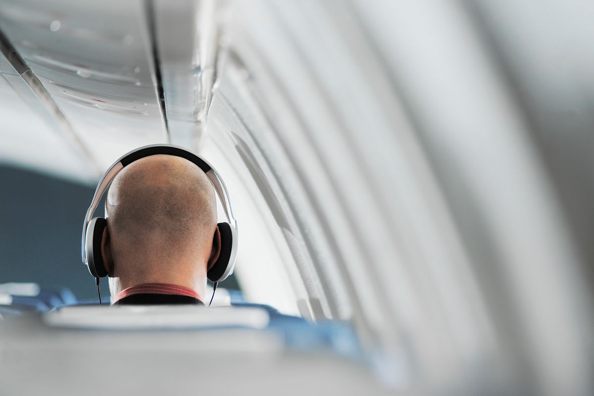Businessman sitting on aeroplane seat, wearing headphones