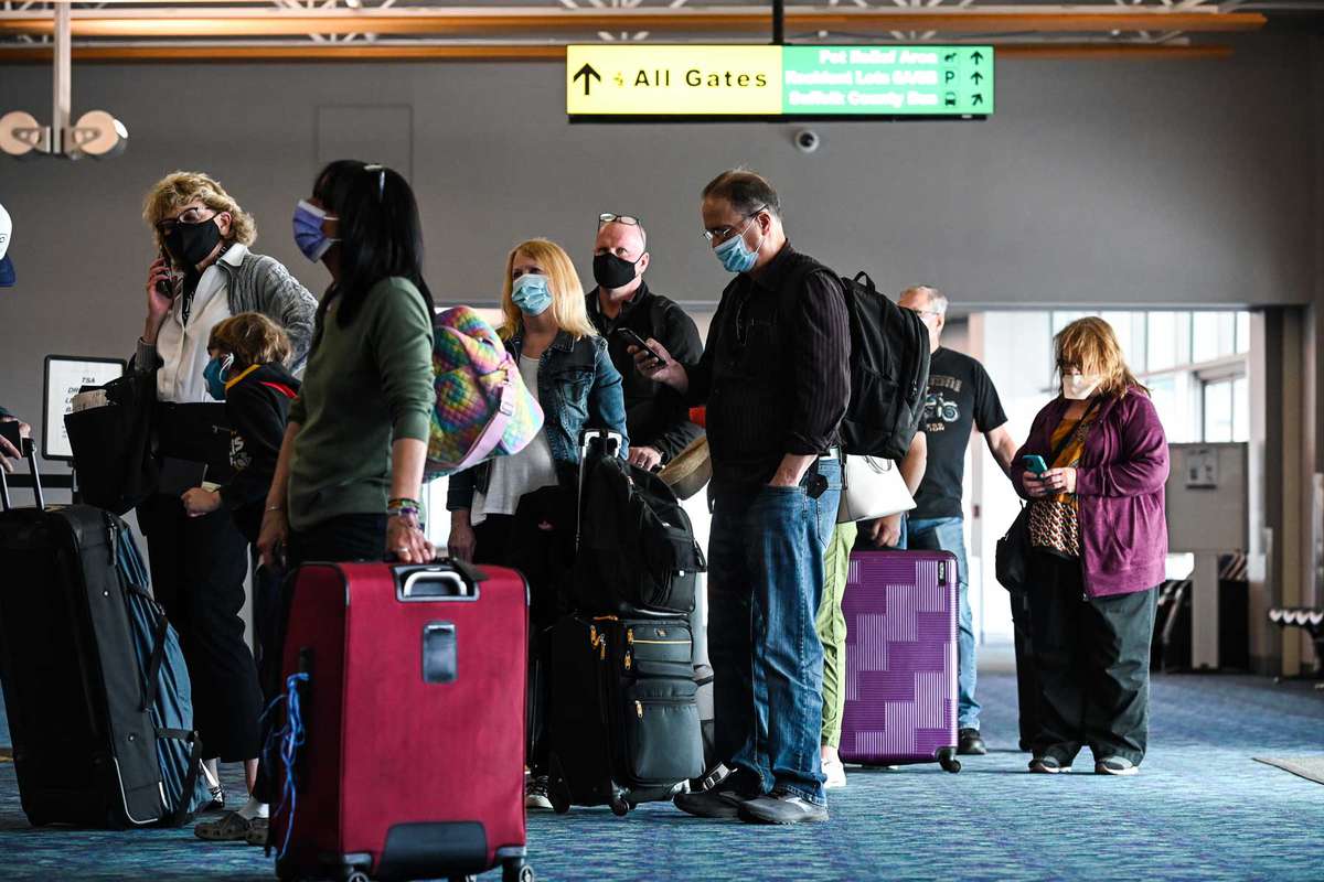 Passengers with face masks wait in line at a Frontier Airlines ticket booth inside the main terminal at Long Island MacArthur Airport, in Ronkonkoma, New York on March 25, 2021.