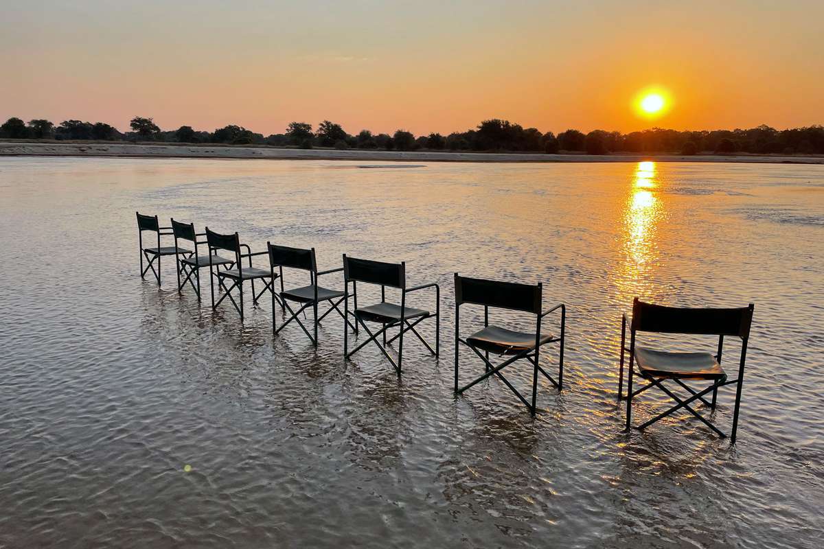 multiple chairs sitting in shallow river overlooking sunset in Zambia