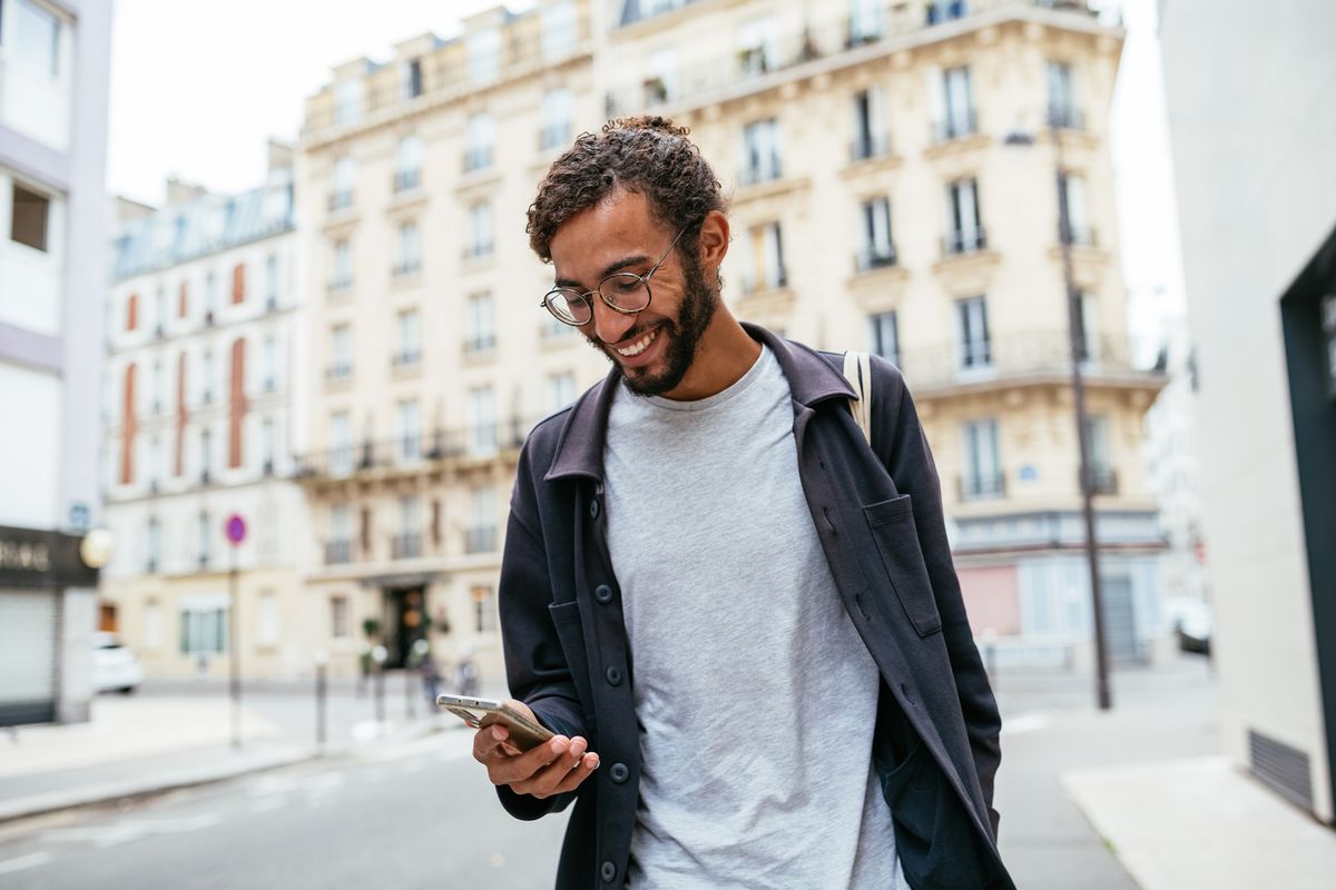 Modern young man with curly hair in the city looking at his smartphone