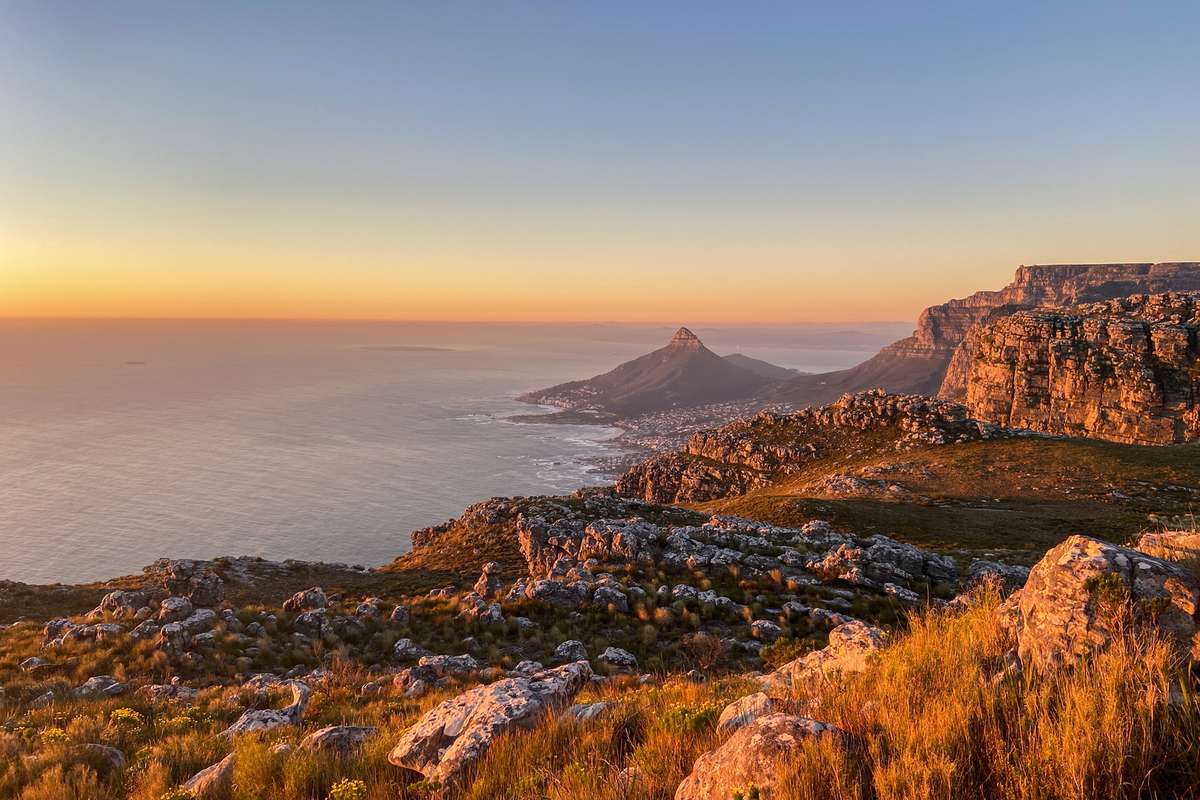 A stunning sunset of the mountains behind Table mountain looking over Camps Bay. Lion's head in the distance over looking the bay