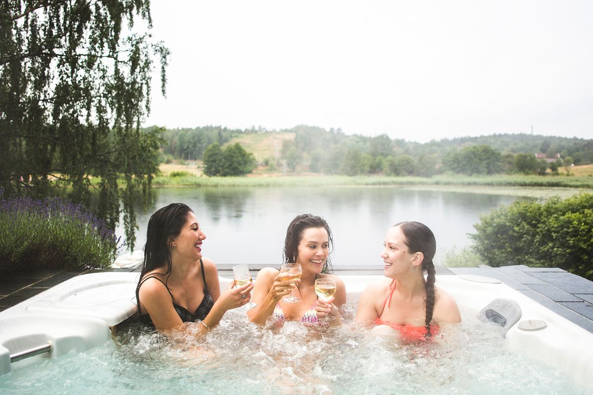 friends enjoying wine in hot tub against lake during weekend getaway