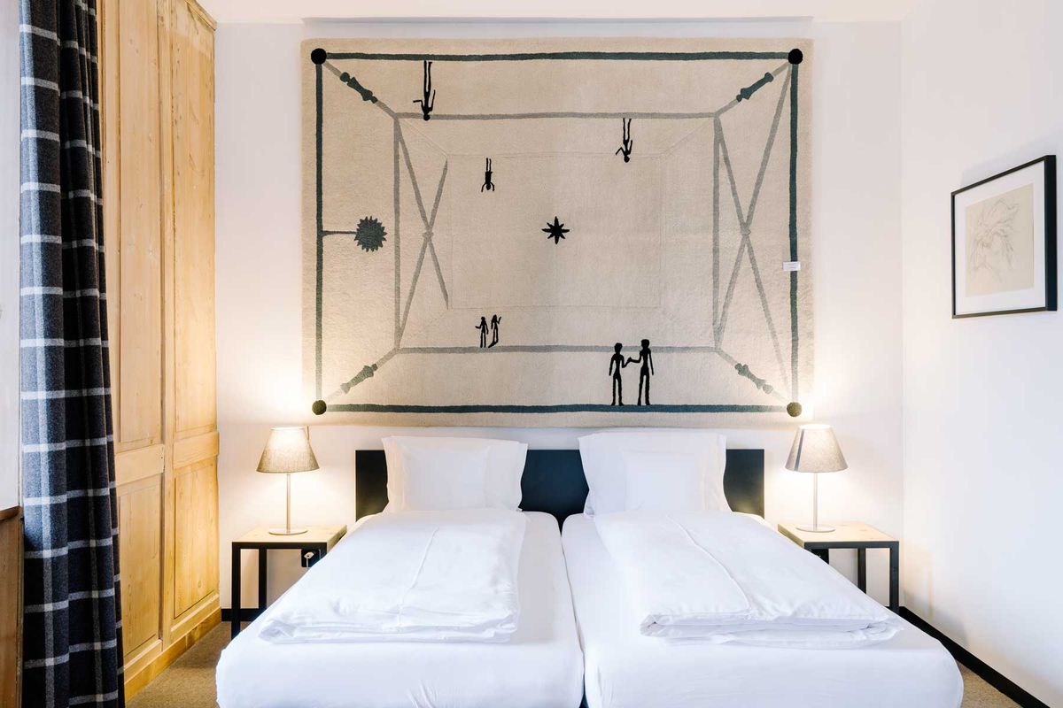 A black and white hotel guest room with a wall hanging by artist Diego Giacometti above the bed