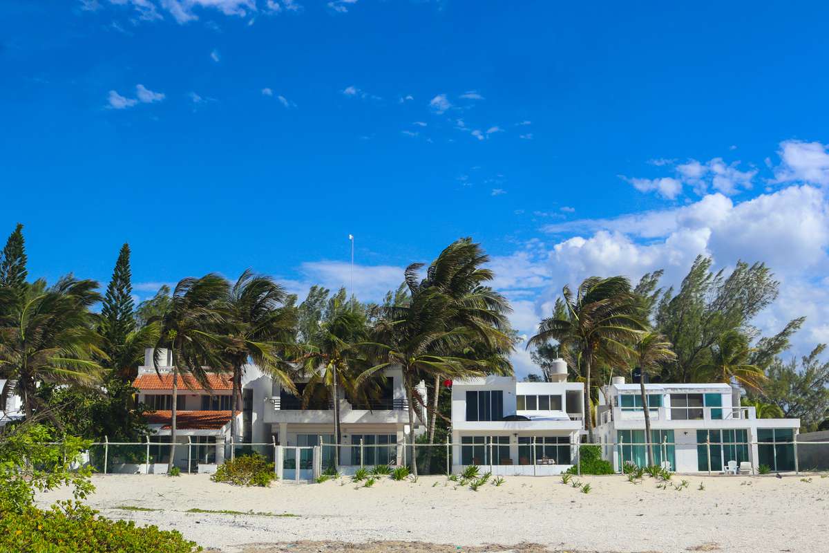 Row of vacation beach houses setting back from the public beach in a Mexican village with bright blue sky and palm trees blowing in the wind