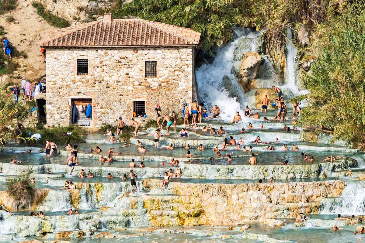 Several people gather and spread out at Cascate del Mulino waterfall and hot springs, Saturnia thermae in Tuscany.
