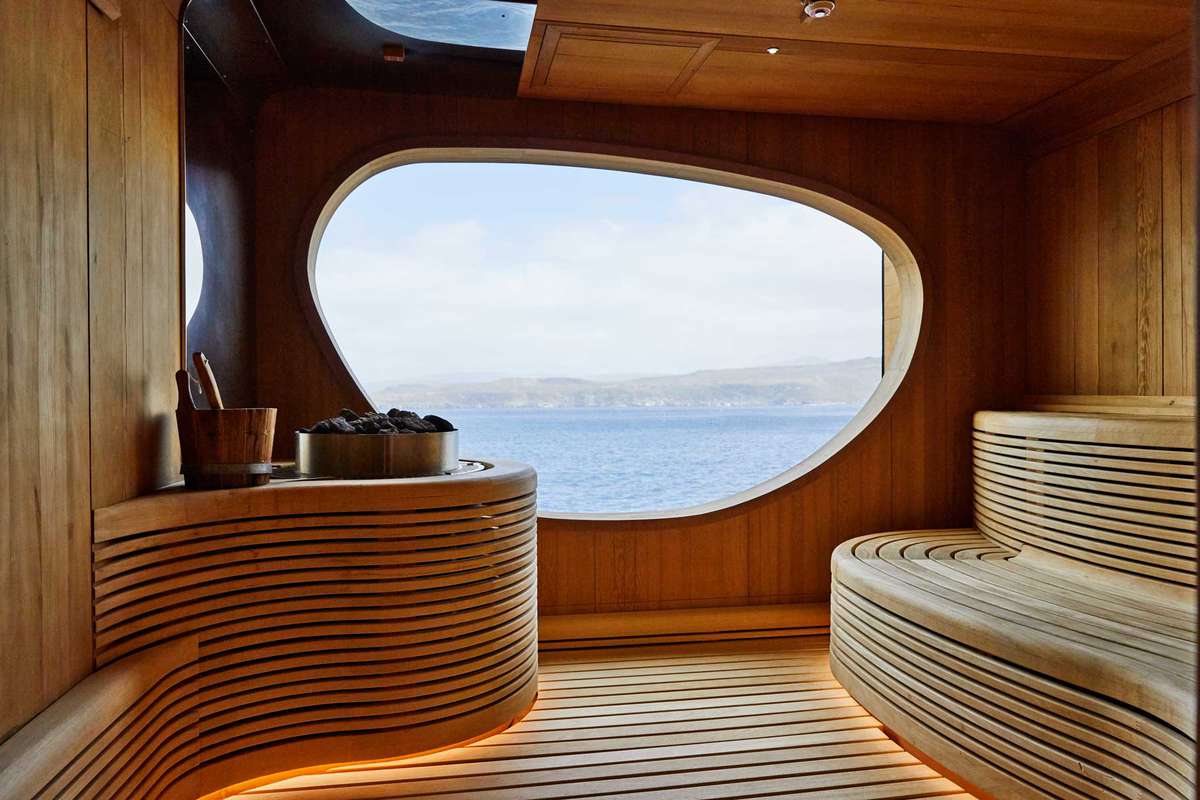 Curved wood design in a sauna on a cruise ship, with a window looking out to water and green hills