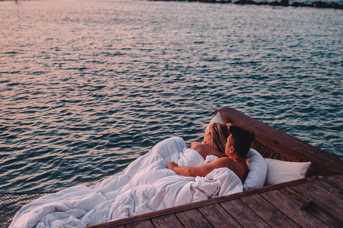 A couple laying in an overwater bed at Renaissance Wind Creek Aruba Resort