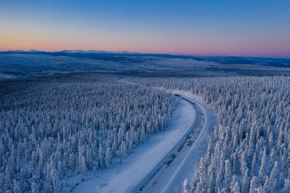 Aerial view at sunset of a vast wintery landscape of pine trees covered in snow off Dalton Highway in Alaska