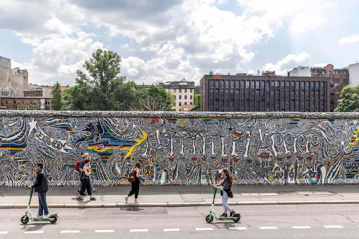 People ride scooters near the East Side Gallery, open-air gallery on the longest surviving section of the Berlin Wall, on July 03, 2021 in Berlin, Germany.