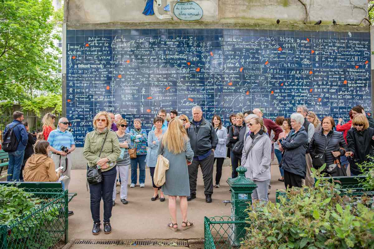 People in a large tour group stop to view the famous I Love You Mural Wall, a popular tourist attraction in the Montmartre neighborhood.
