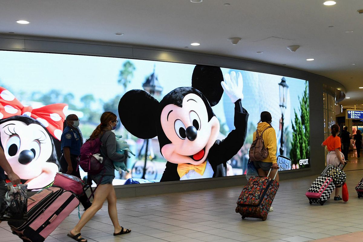Travelers walk past a sign advertising Walt Disney World at Orlando International Airport