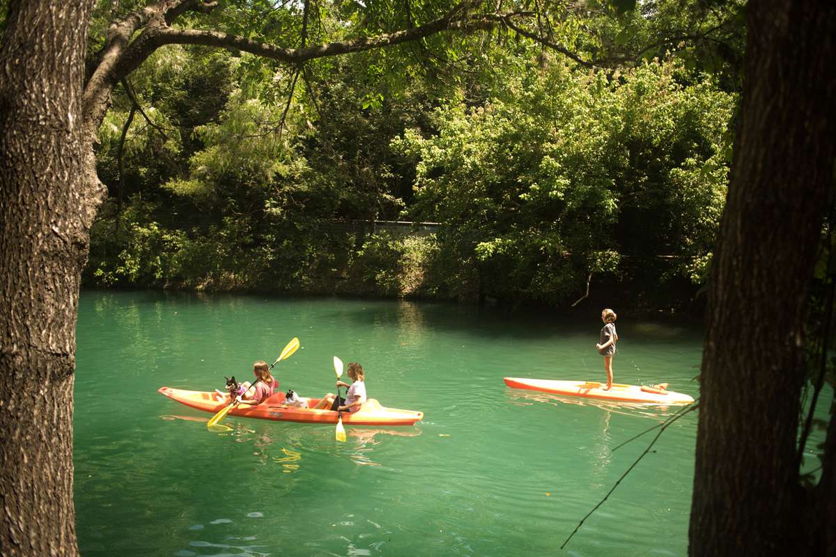 Friends canoeing with dogs and paddleboarding in Barton Creek at Zilker Park in Austin
