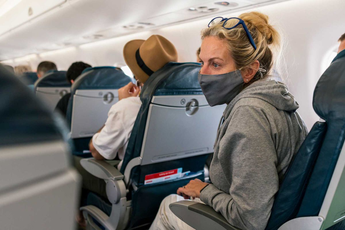 Woman sitting on a plane wearing a protective face mask to reduce the spread of COVID-19. She is looking away from the camera with glasses on her head.