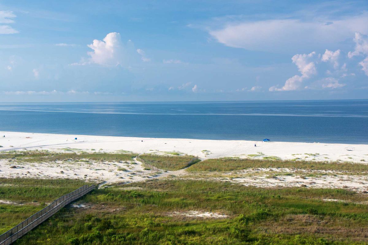 Aerial view of beach coastline and boardwalk on Dauphin Island in Alabama on a sunny blue sky day