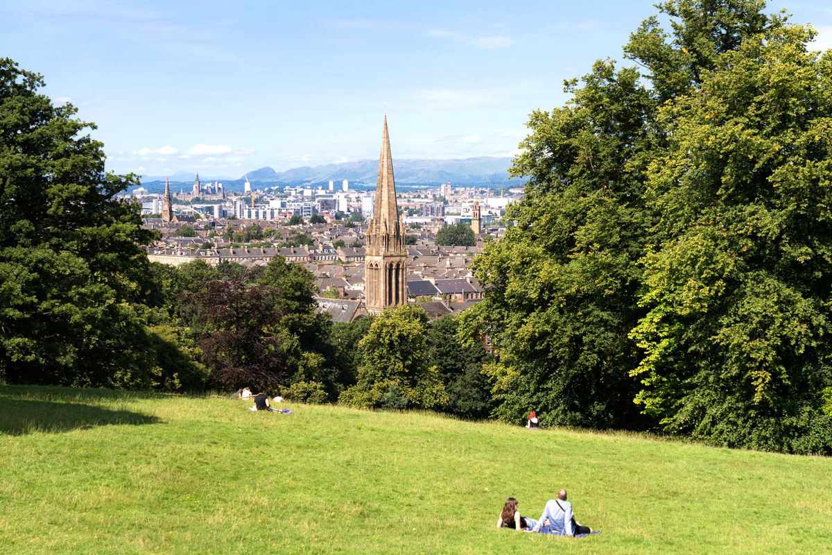 People relaxing on a hill in Queen's Park, with a view over the city during sunny weather.