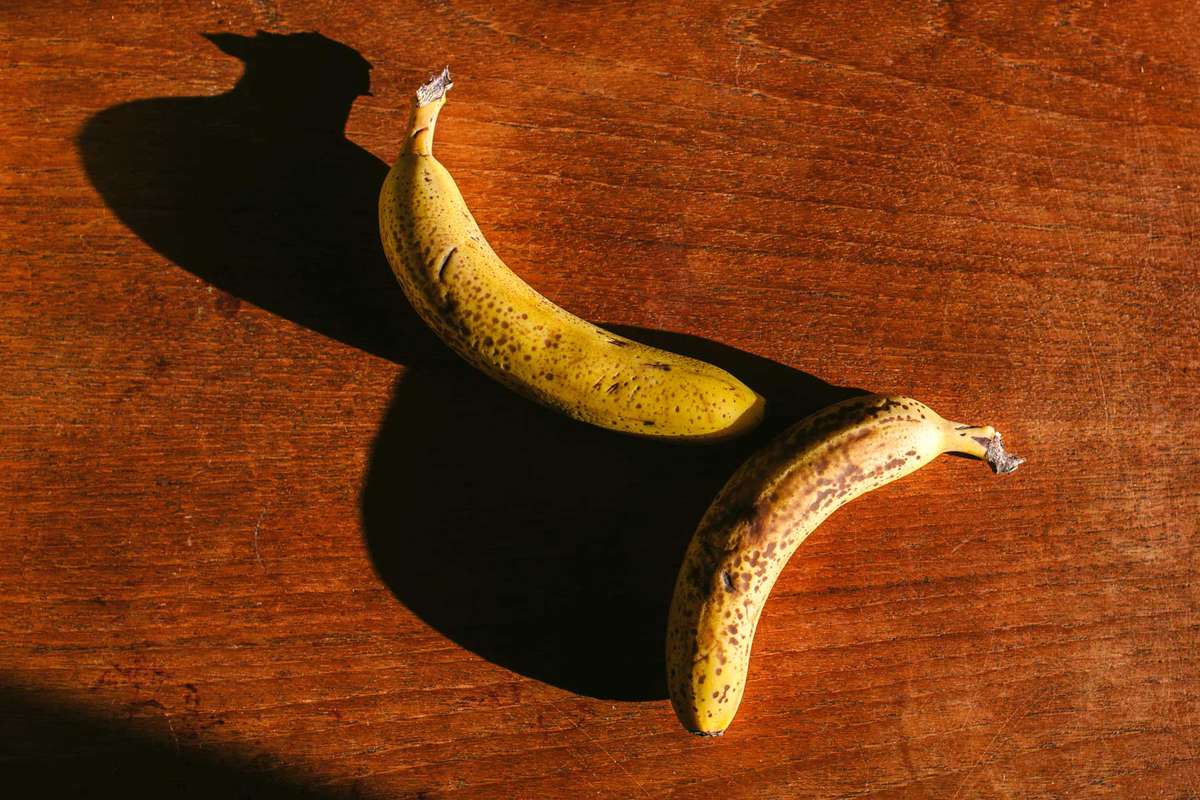 Two past their best bananas lie side by side on a wooden table