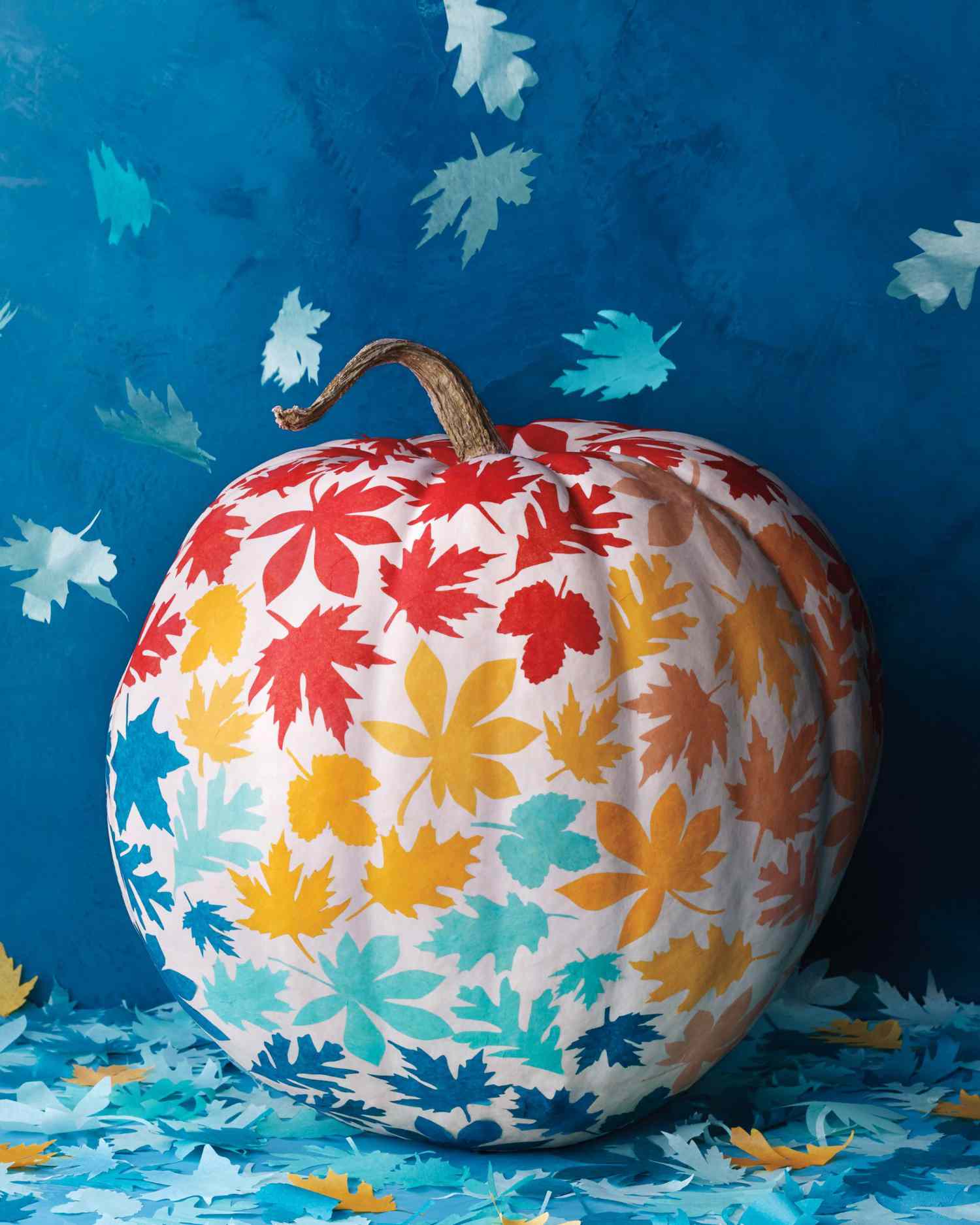 white pumpkin with painted leaves in red yellow light and dark blue