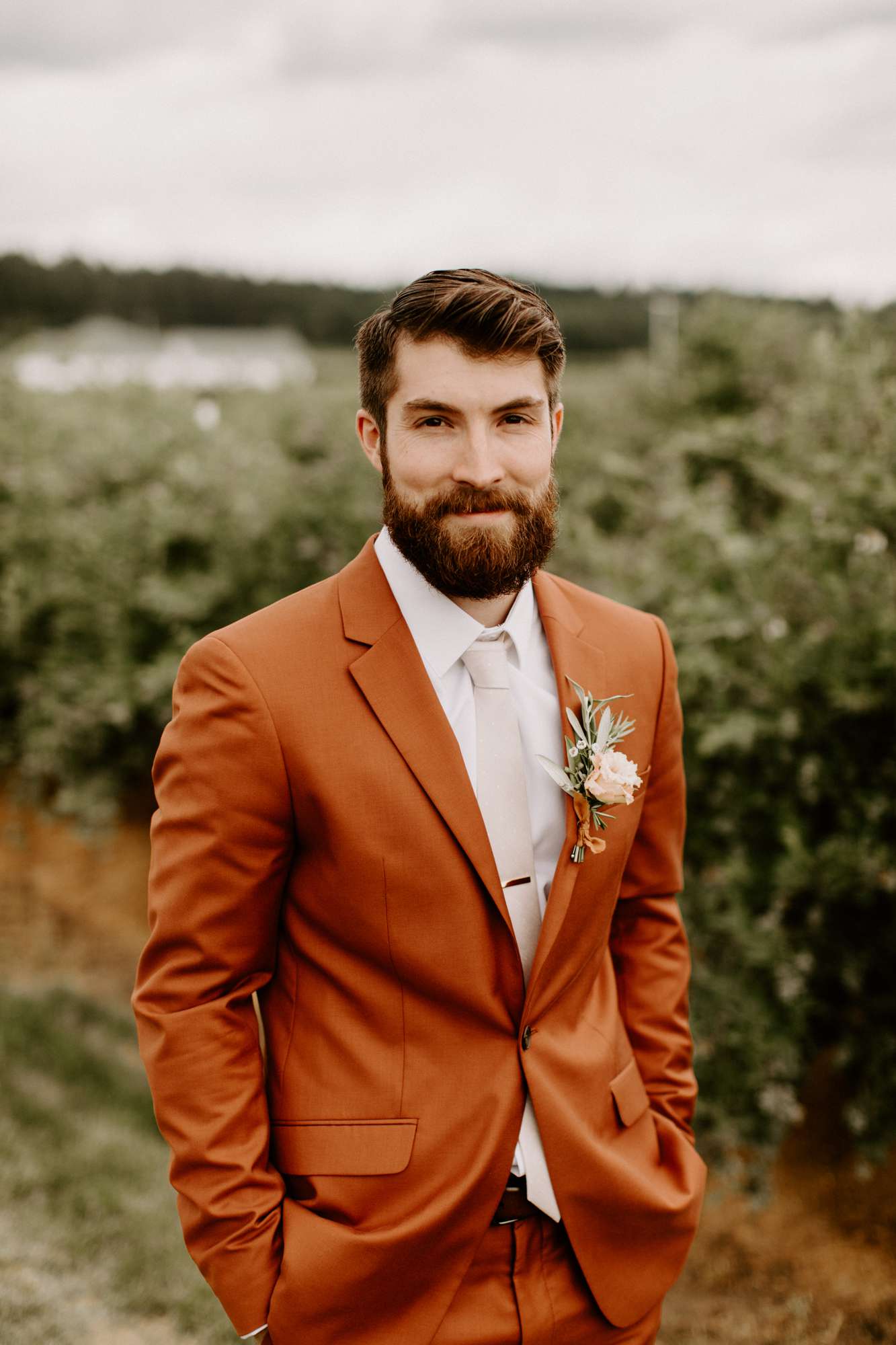 groom in burnt orange wedding suit outside
