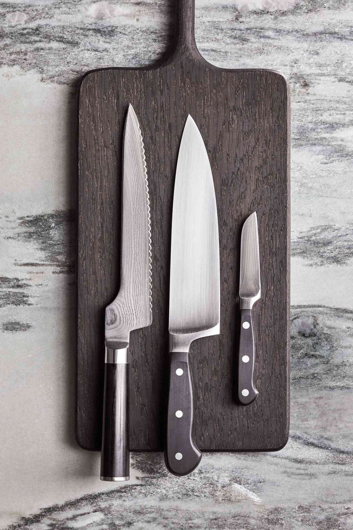 three knives on a dark grey cutting board