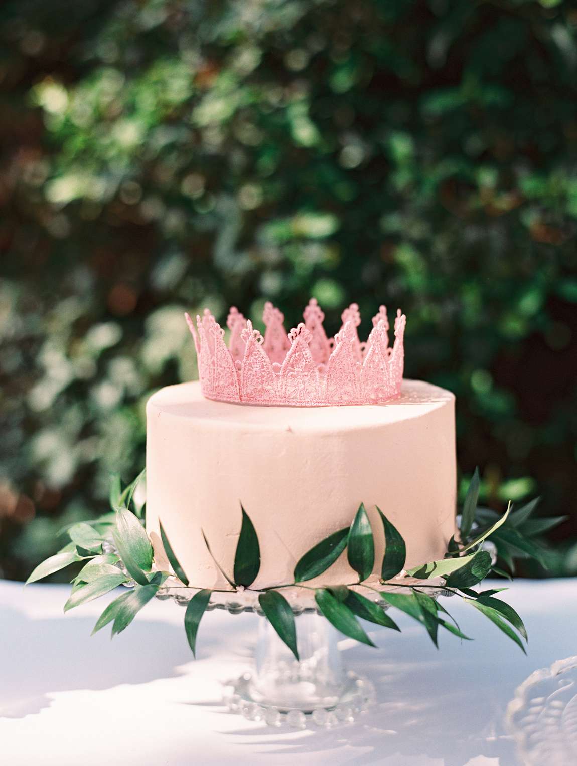 pink lace crown single layered pink frosted cake with greenery accent