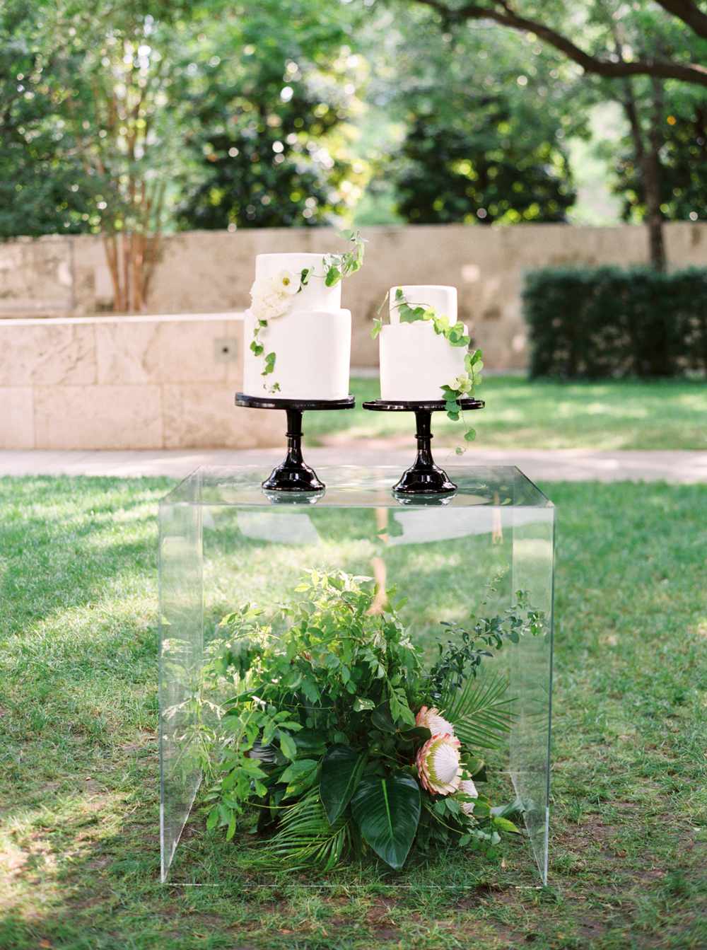 lucite table containing a floral arrangement displaying two white wedding cakes