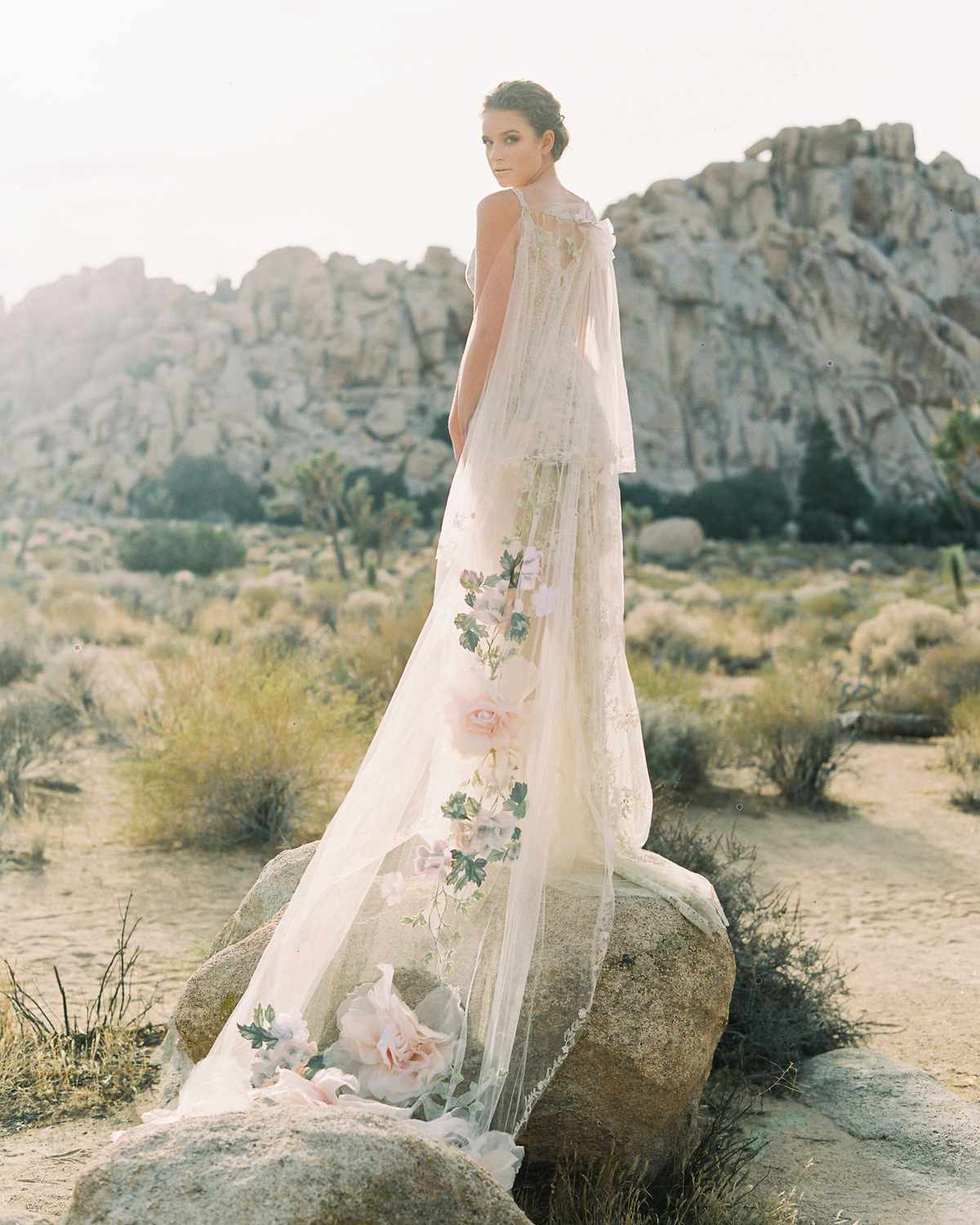 bride wearing long train lace wedding dress outside standing on rock with flowers