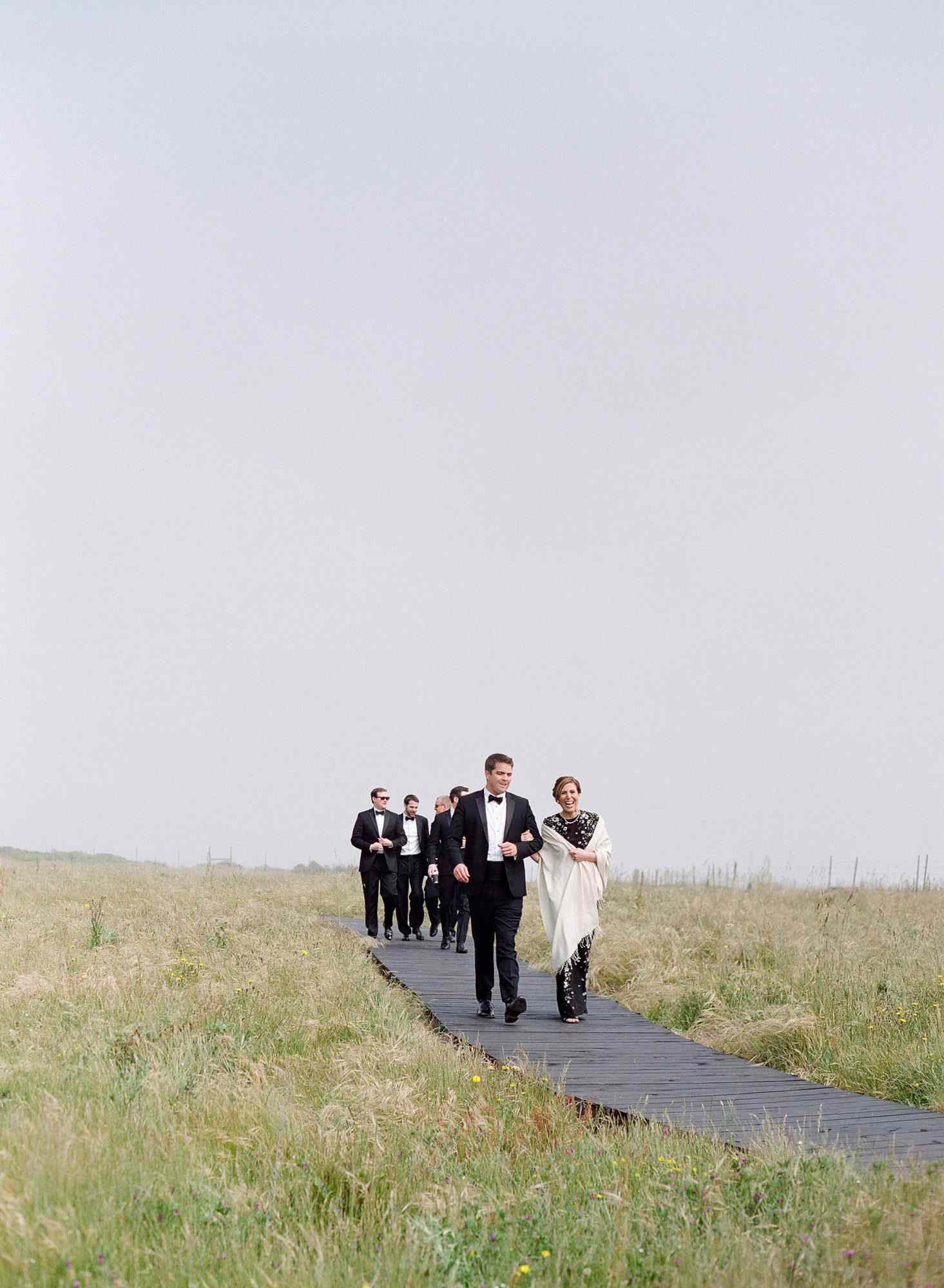 whitney zach wedding guests walking down wooden path in field
