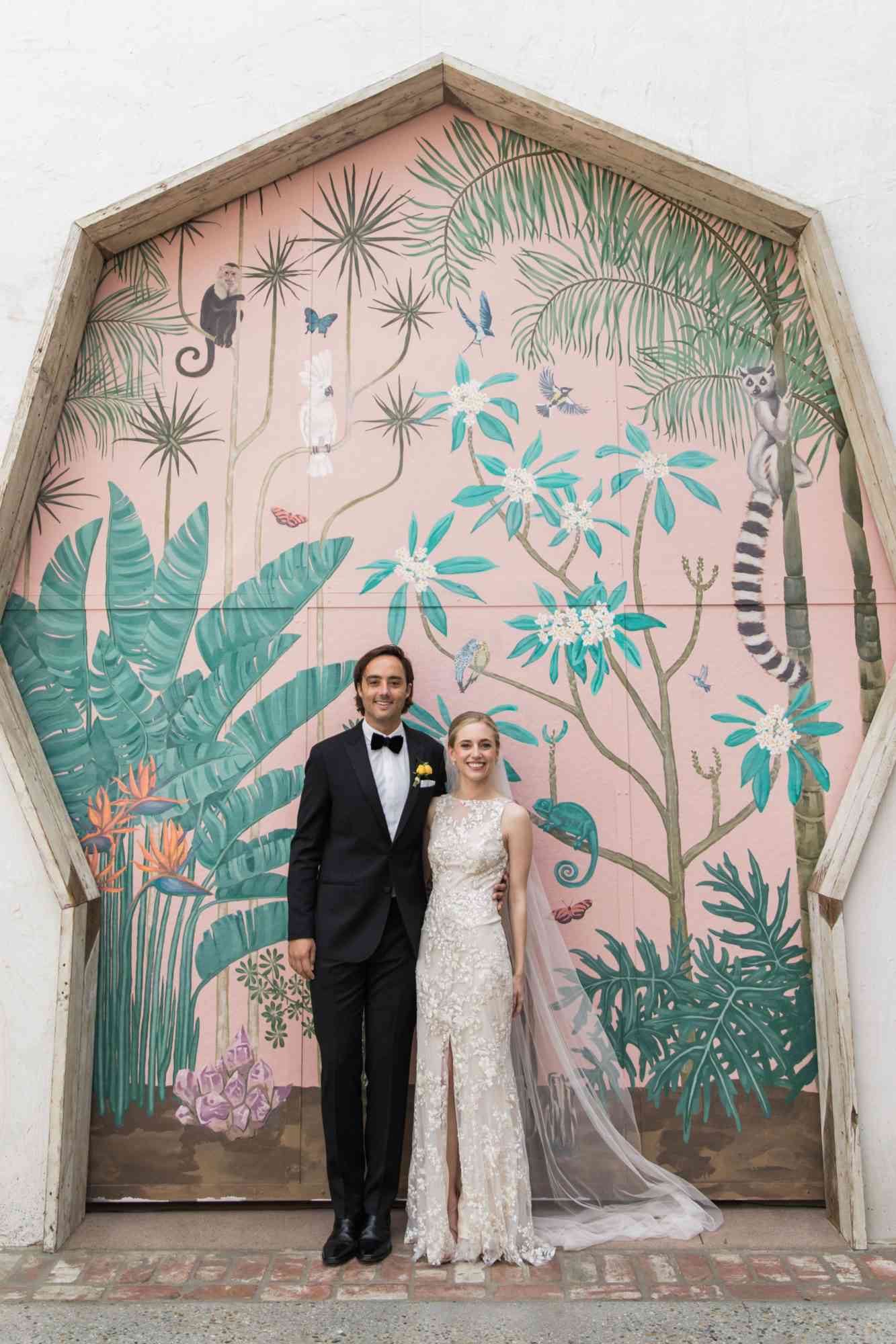 bride and groom pose in wedding attire in front of painted wall
