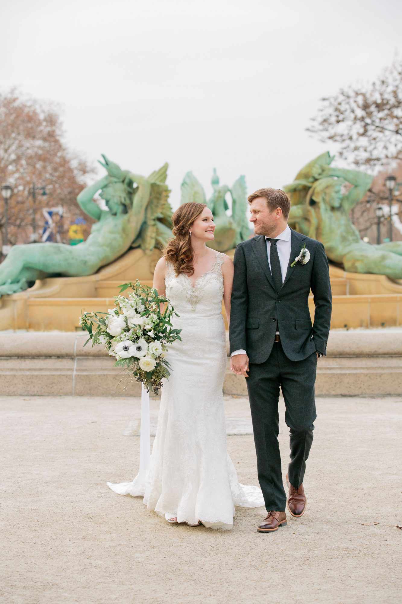 bride and groom smile at each other in front of fountain