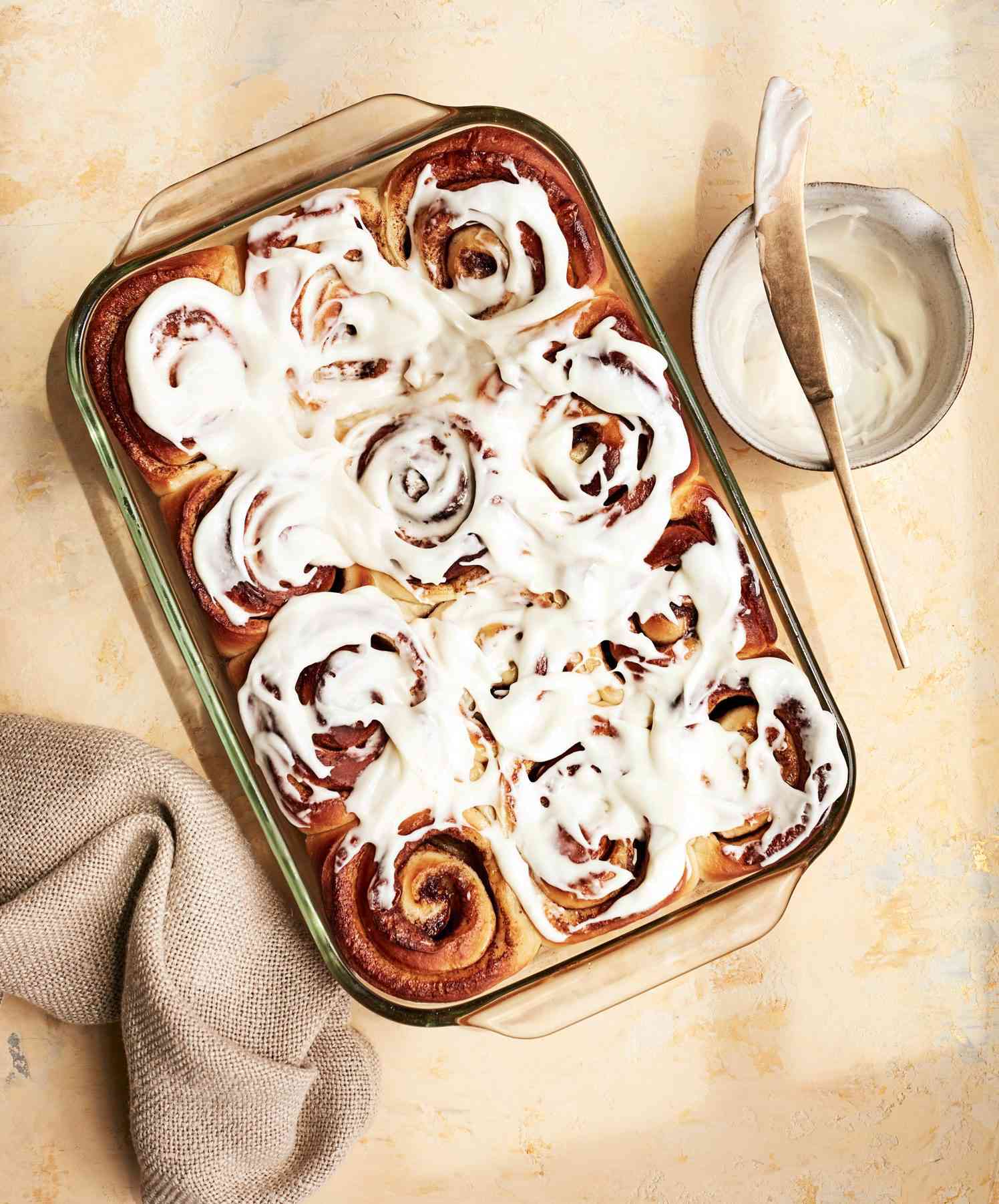 cinnamon rolls in glass pan with bowl of frosting