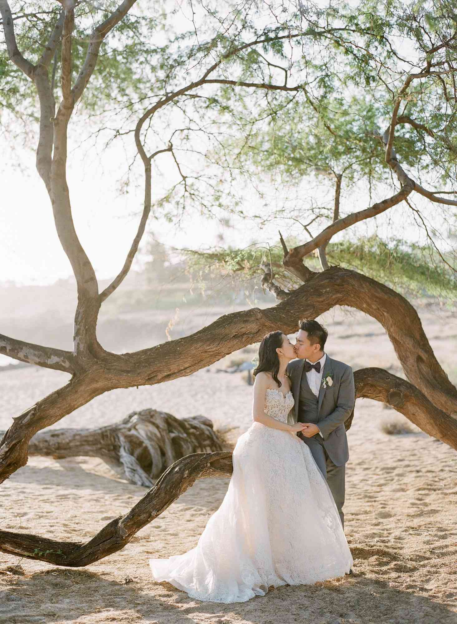bride and groom hawaiian wedding kiss by beach tree