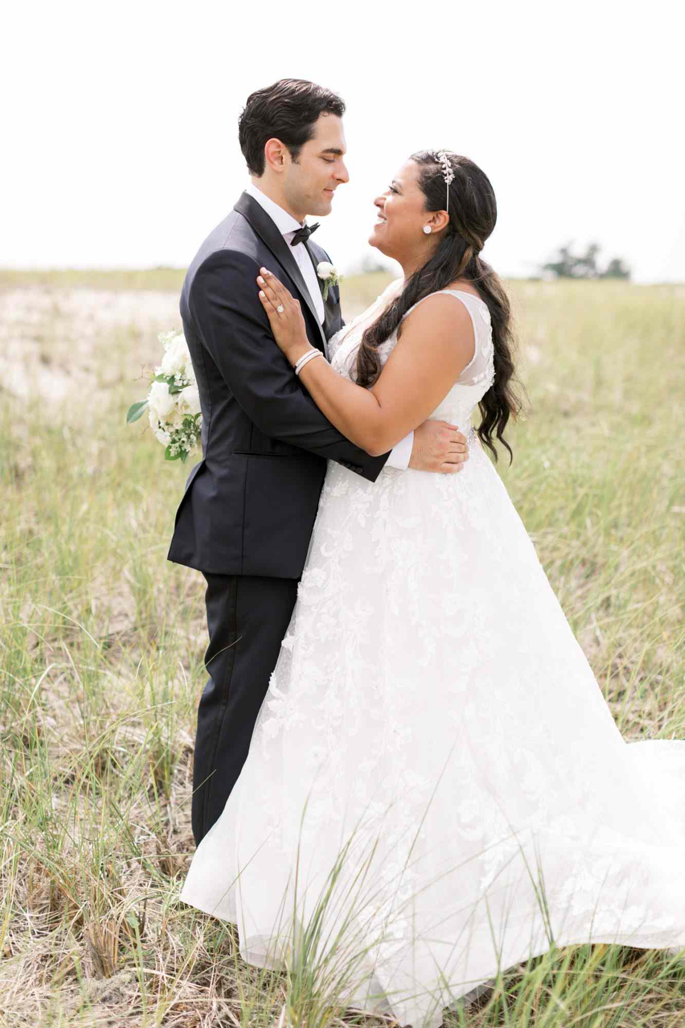bride and groom smiling at one another in field of tall grass