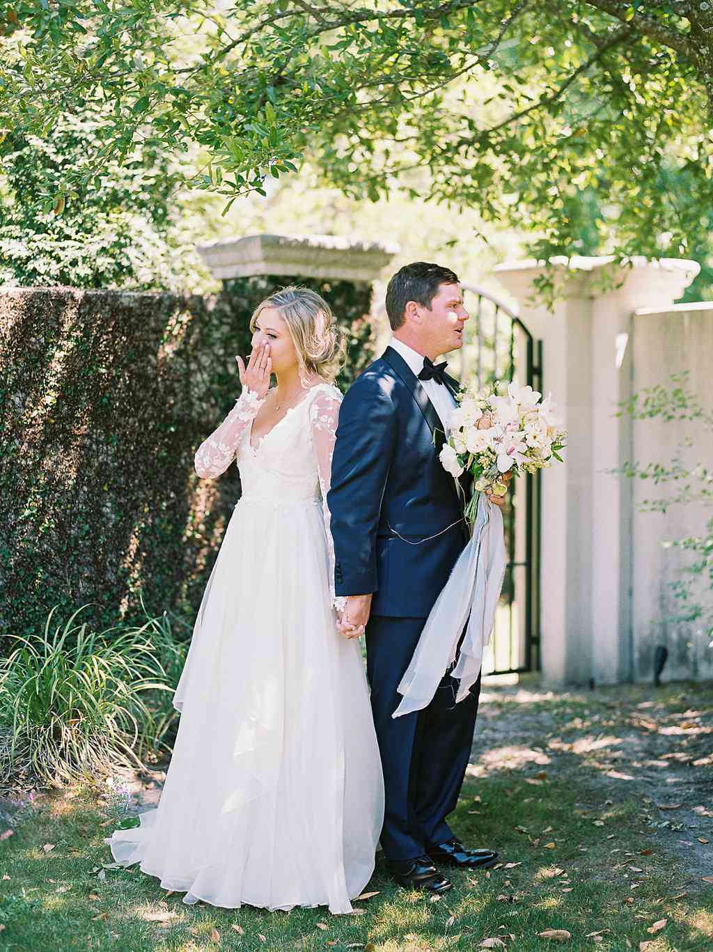 bride and groom sharing tearful first look in front of wall of greenery