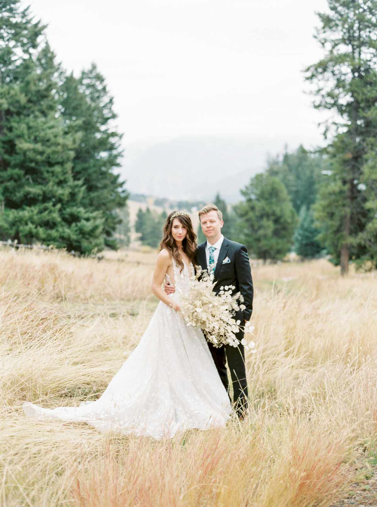 bride and groom in field with pine trees in background