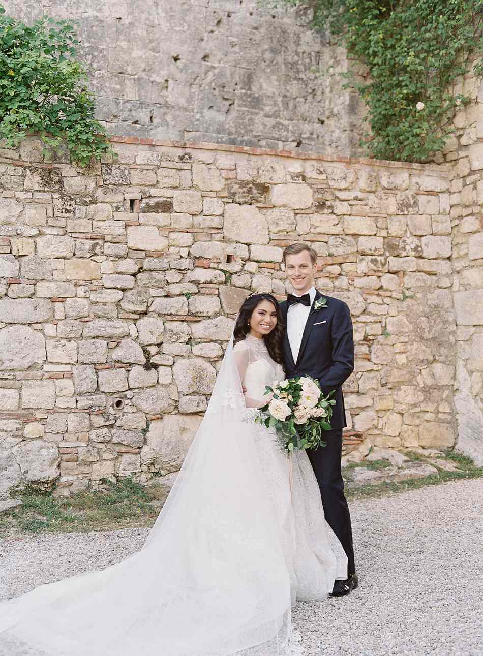 bride and groom pose in front of stone wall