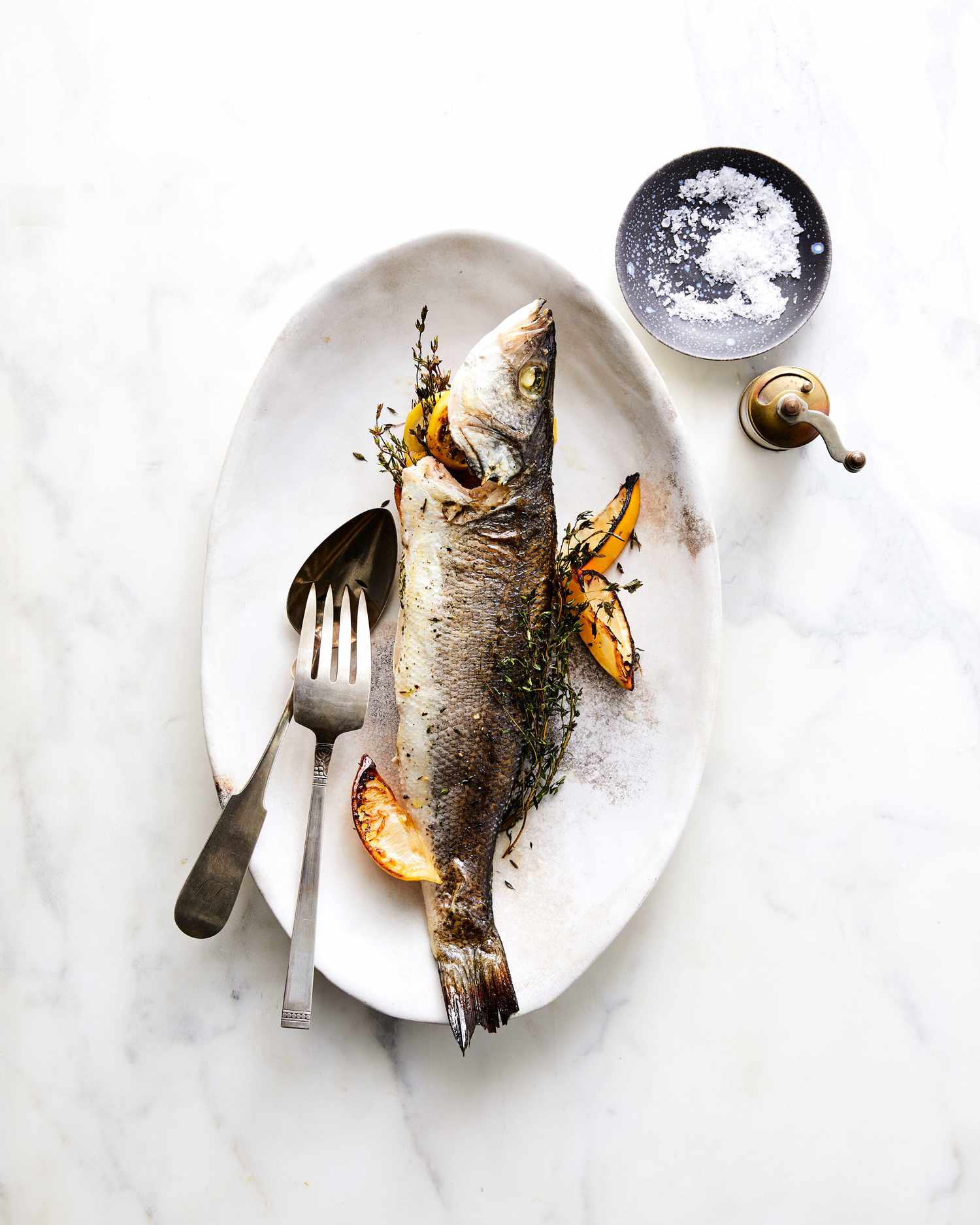 Whole-Roasted Branzino with Lemon and Thyme on plate with lemon wedges and silverware