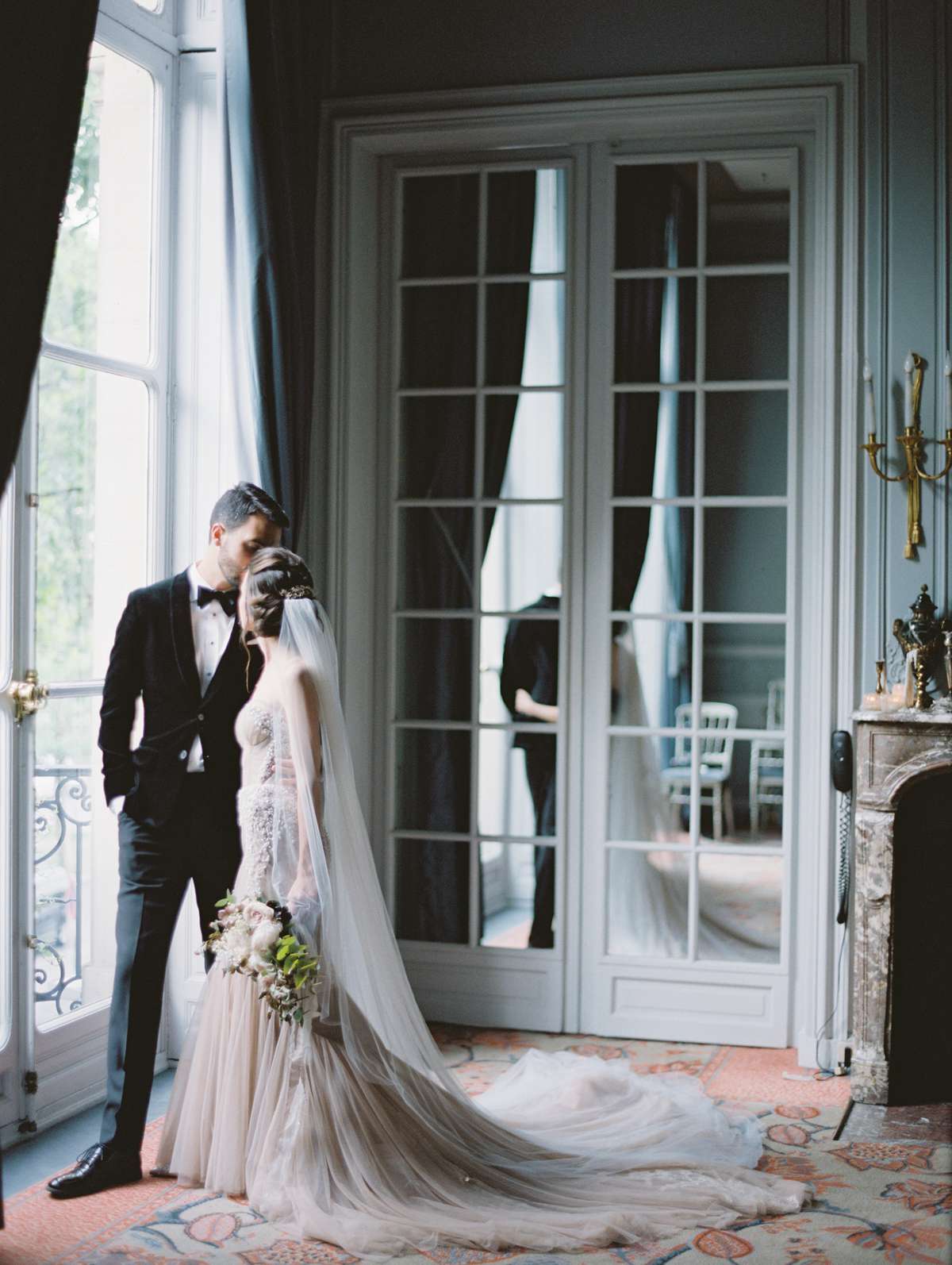 bride and groom kissing near window in parisian salon