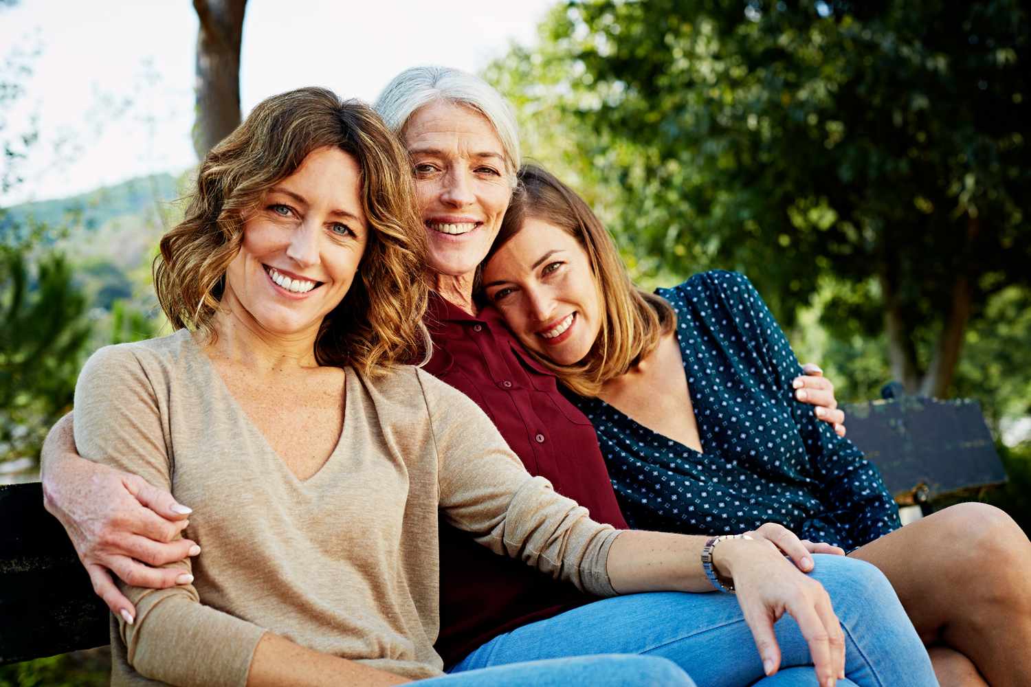 Portrait of happy mother sitting with daughters on park bench