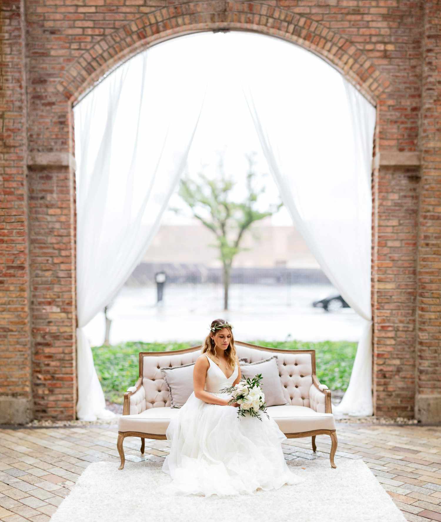 bride sitting on white couch below brick arch