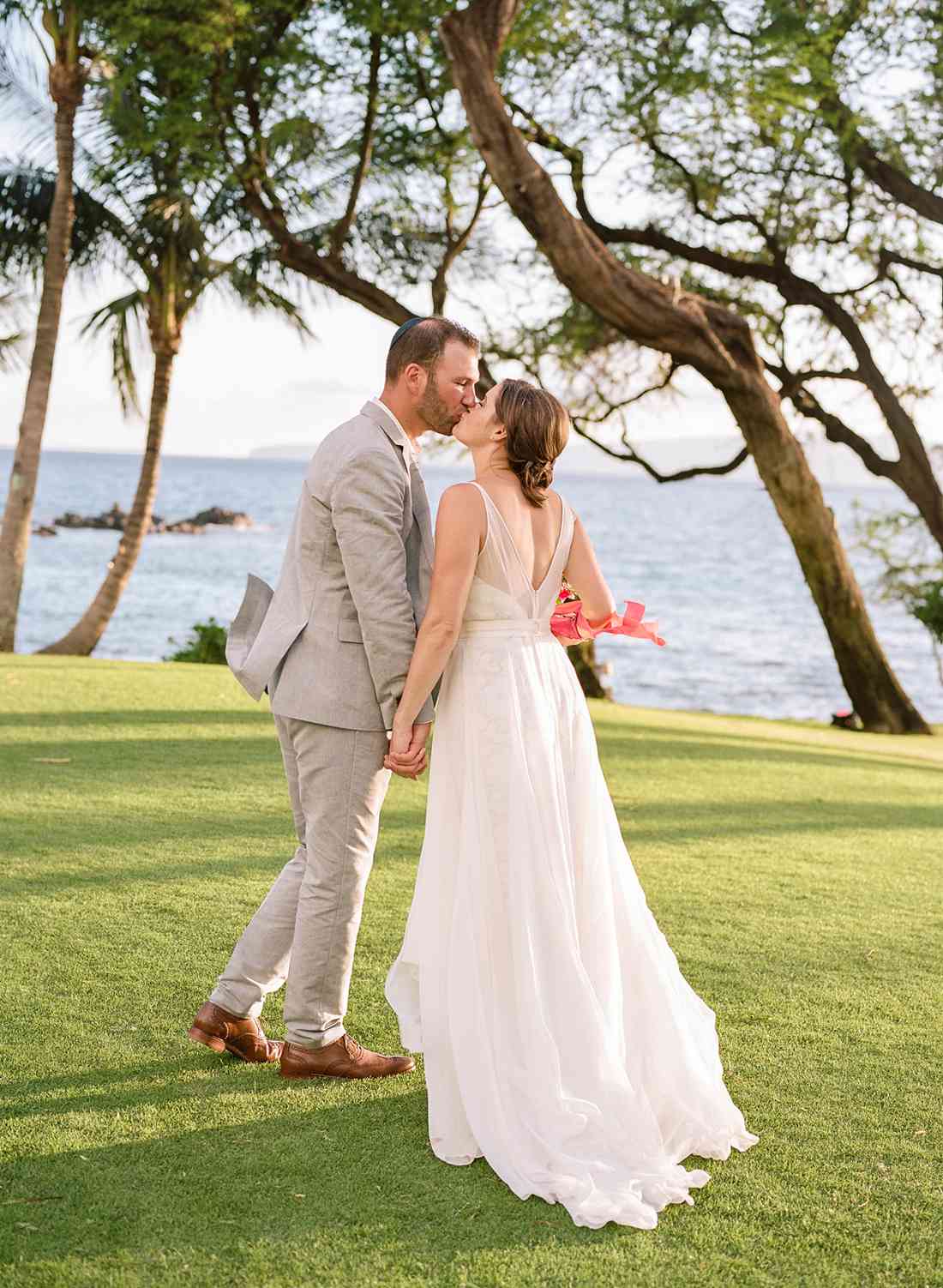 bride and groom hold hands while kissing on green lawn