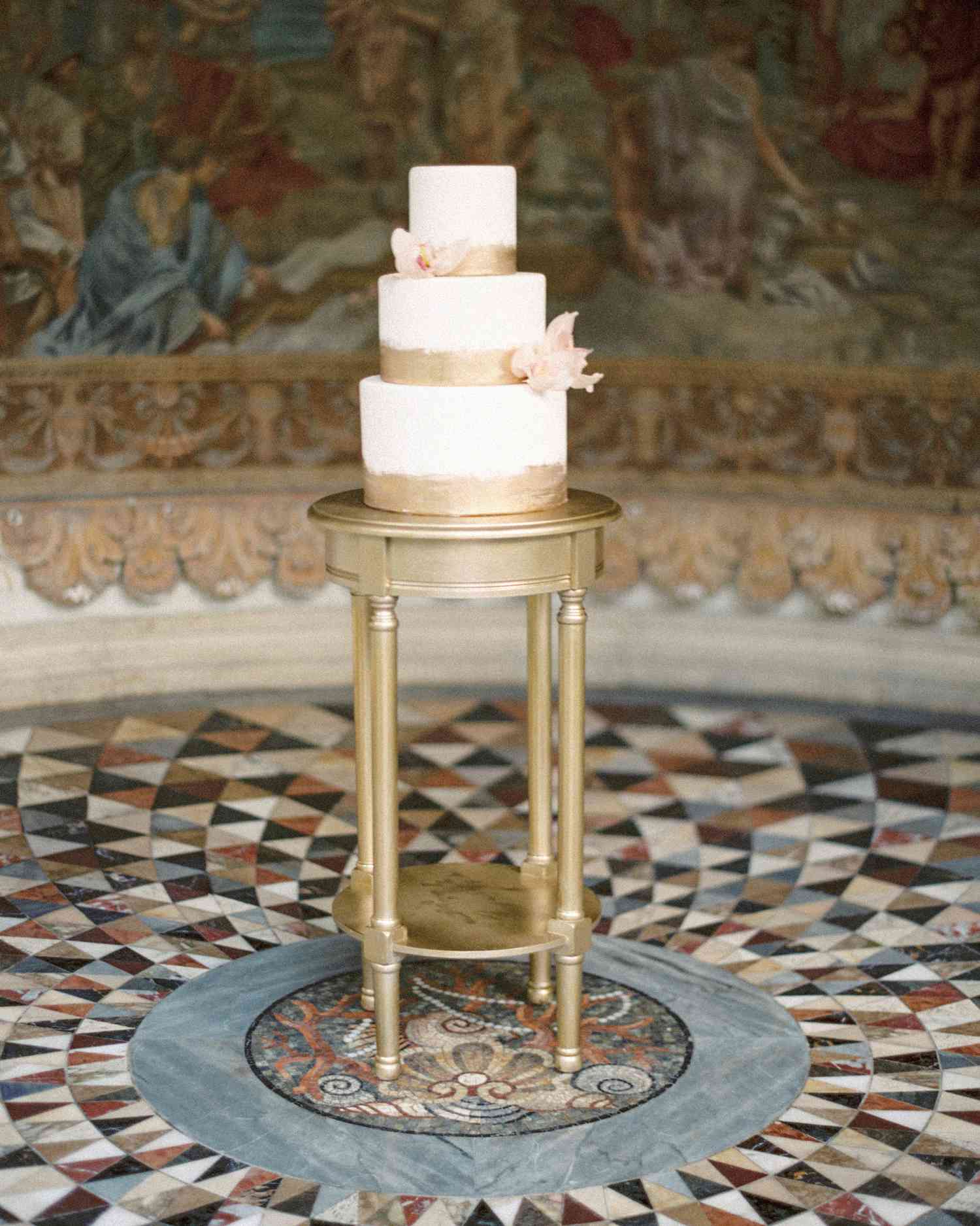 three tiered white wedding cake with gold foil accents and orchid decor