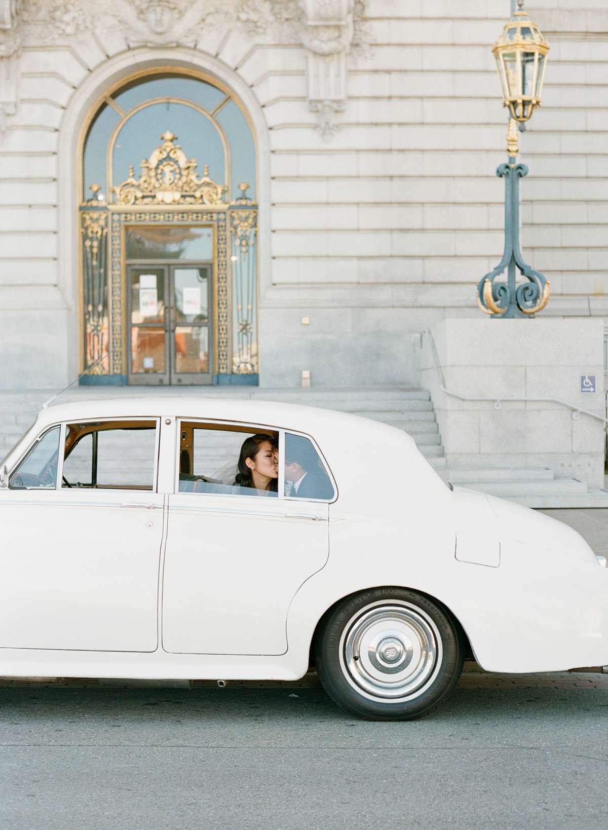 bride and groom sitting in back of white vintage getaway car