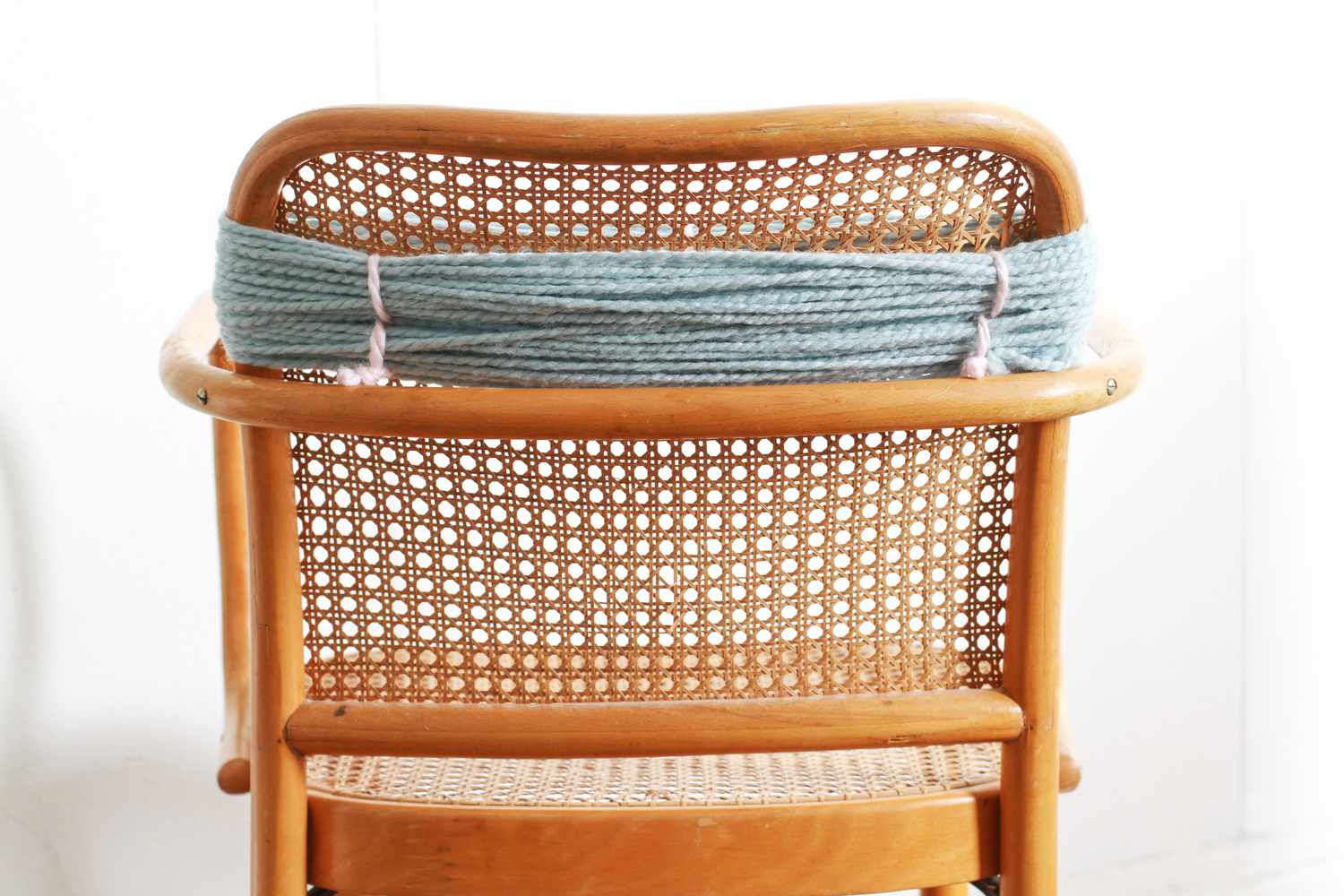 blue yarn wrapped around back of chair tied with white yarn pieces