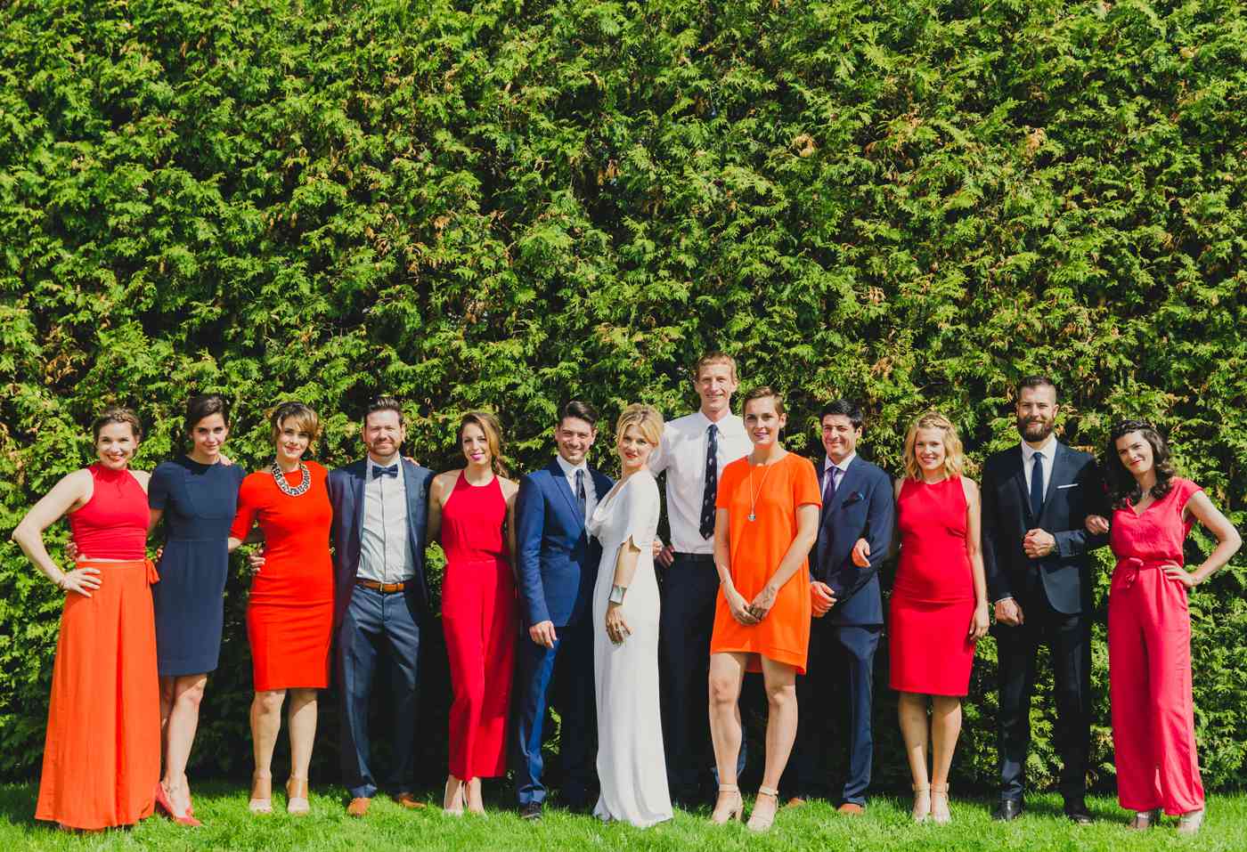wedding party standing in front of hedges featuring women wearing mismatched bridesmaids jumpsuits