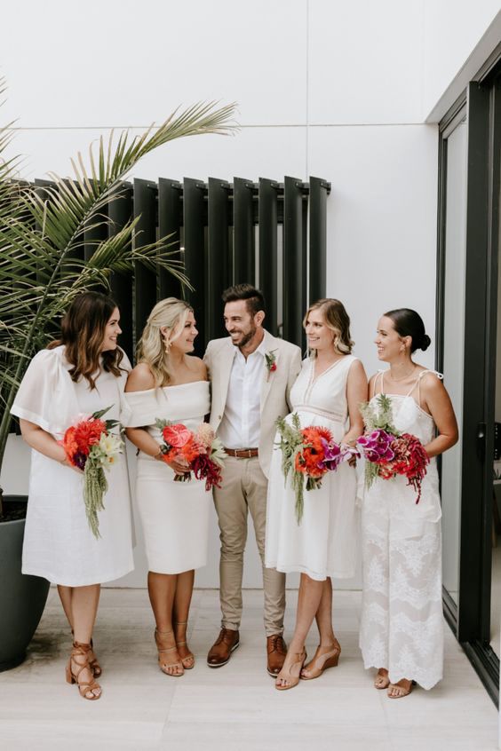 women standing with groom wearing mismatched white bridesmaids dresses and jumpsuit
