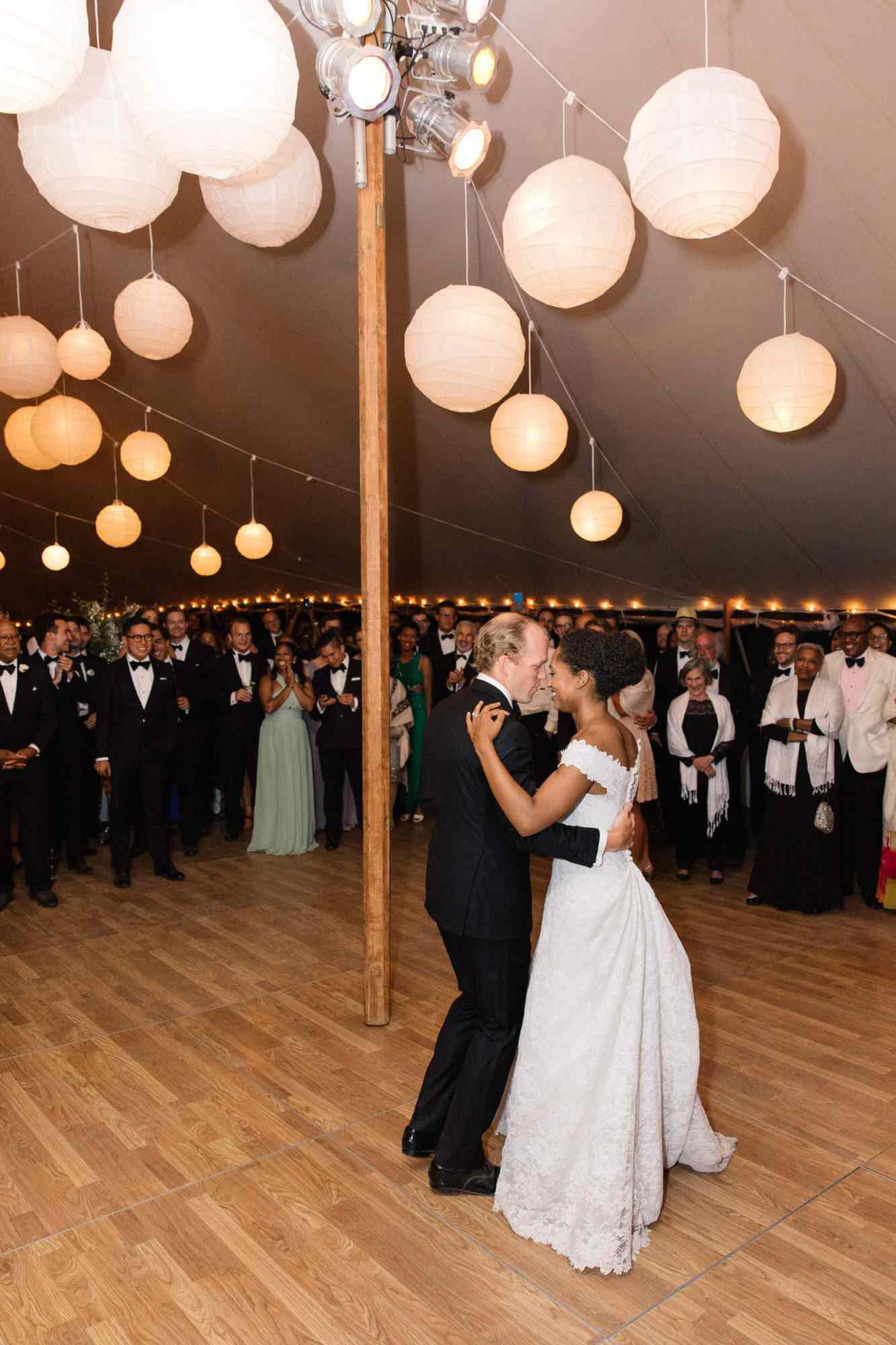 bride and groom share first dance surrounded by guests under hanging lanterns